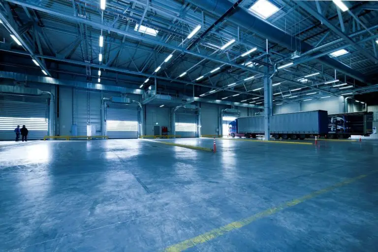 Home Wide view of an empty modern warehouse with industrial lighting and trucks.