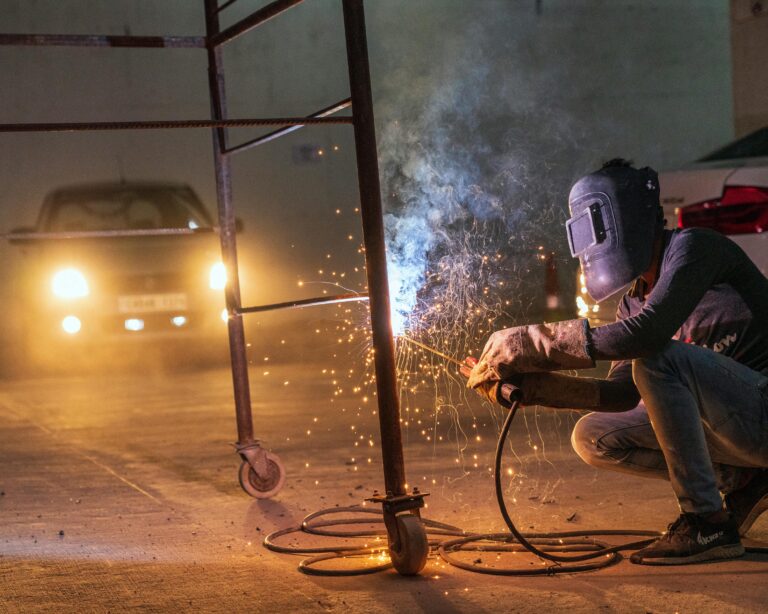 A welder at work with sparks flying in an industrial setting during night time.